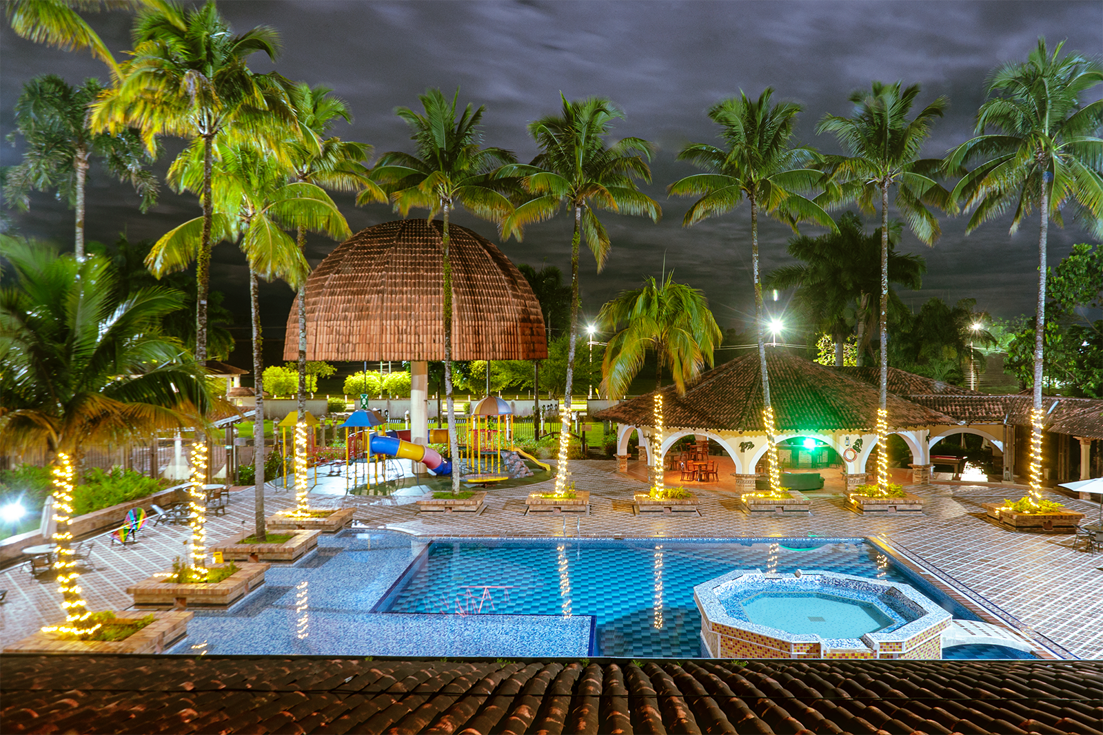 Tequendama Hotel Campestre Villavicencio: Pool, playground, & palm trees at night.