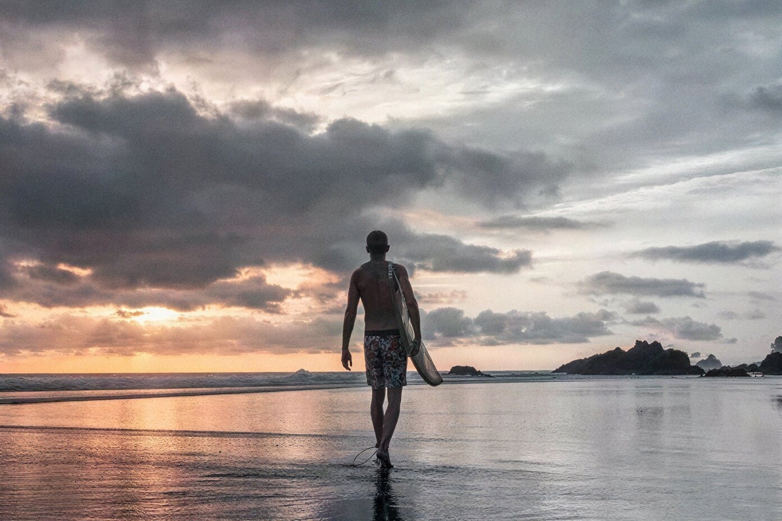 Surfero camina al atardecer en playa; ideal para Tequendama Corporativa.