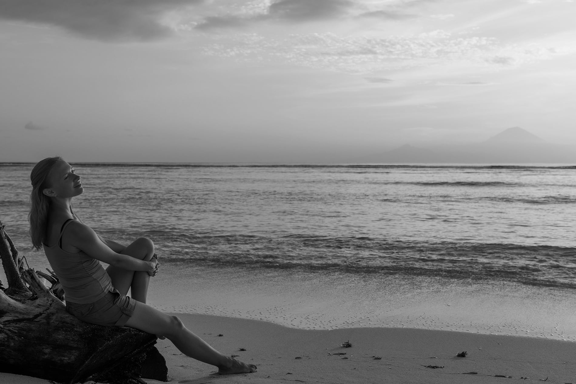 Mujer en playa al atardecer, vista al mar y montañas distantes. Ideal para Tequendama: Corporativa.=s1900