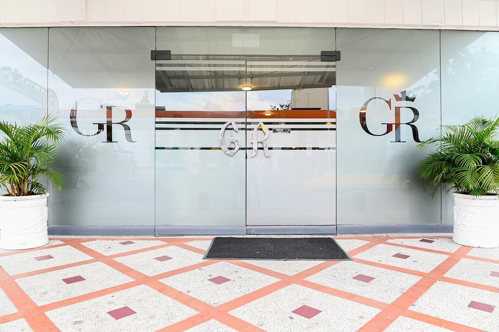Modern glass entrance to Tama Hotel Granada Real, with potted plants and patterned flooring.