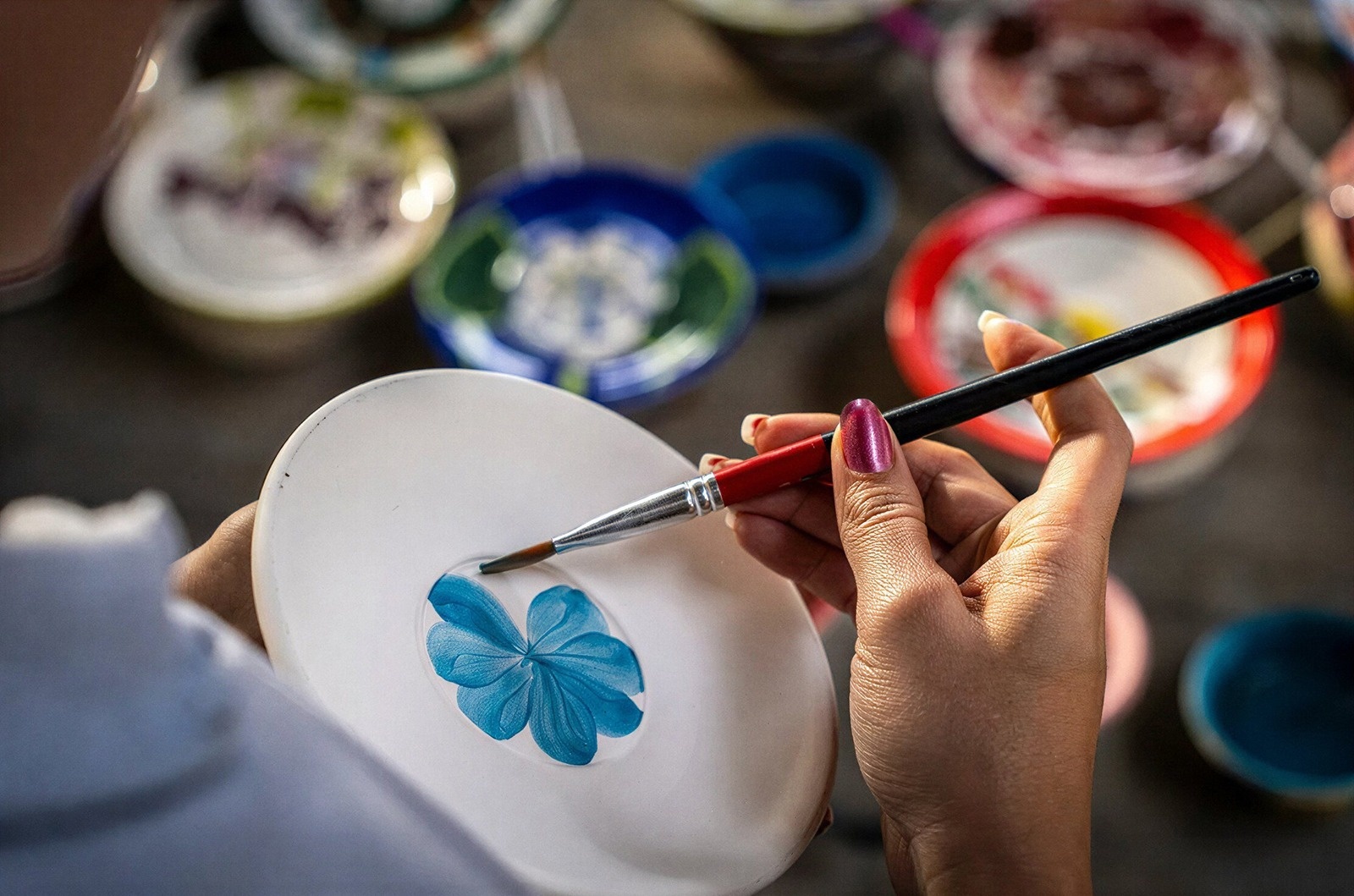Tequendama: Corporativa. Manos pintando flor azul en plato, detalle artesanal