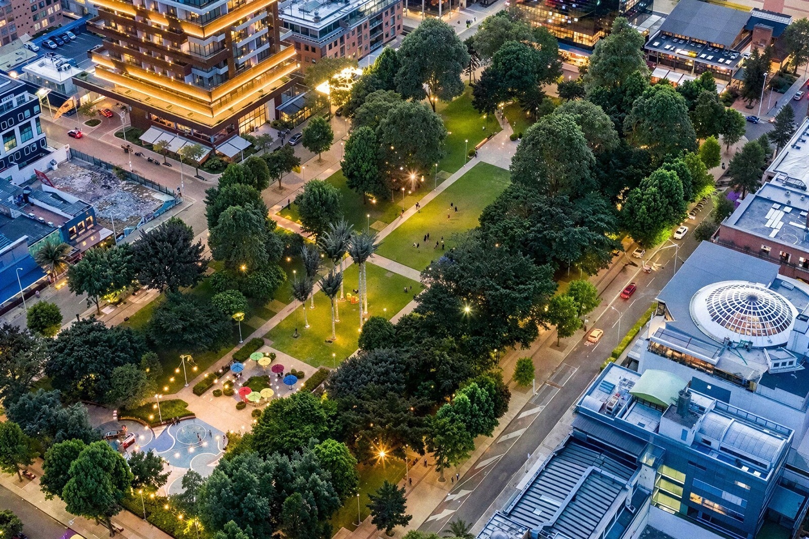Vista aérea de Tequendama: Corporativa, parque urbano iluminado con gente y edificios modernos.