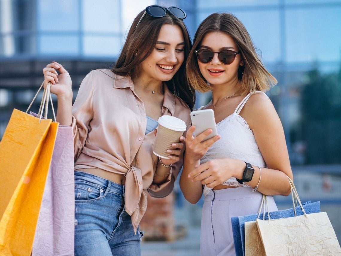 Dos mujeres con bolsas de compras y café, disfrutando de Tequendama: Corporativa.