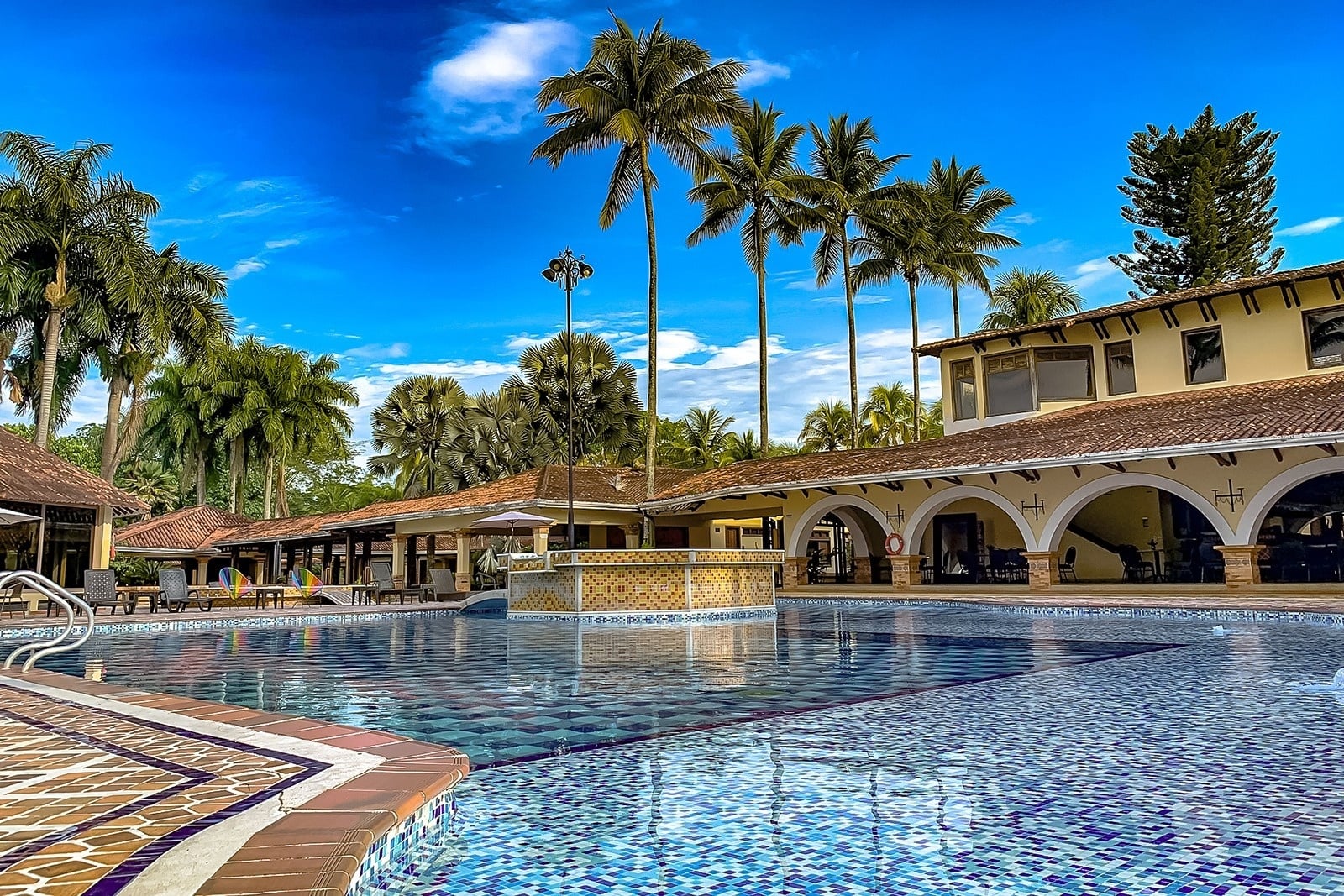 Tequendama Hotel Campestre Villavicencio: Poolside paradise with palms and vibrant blue sky.