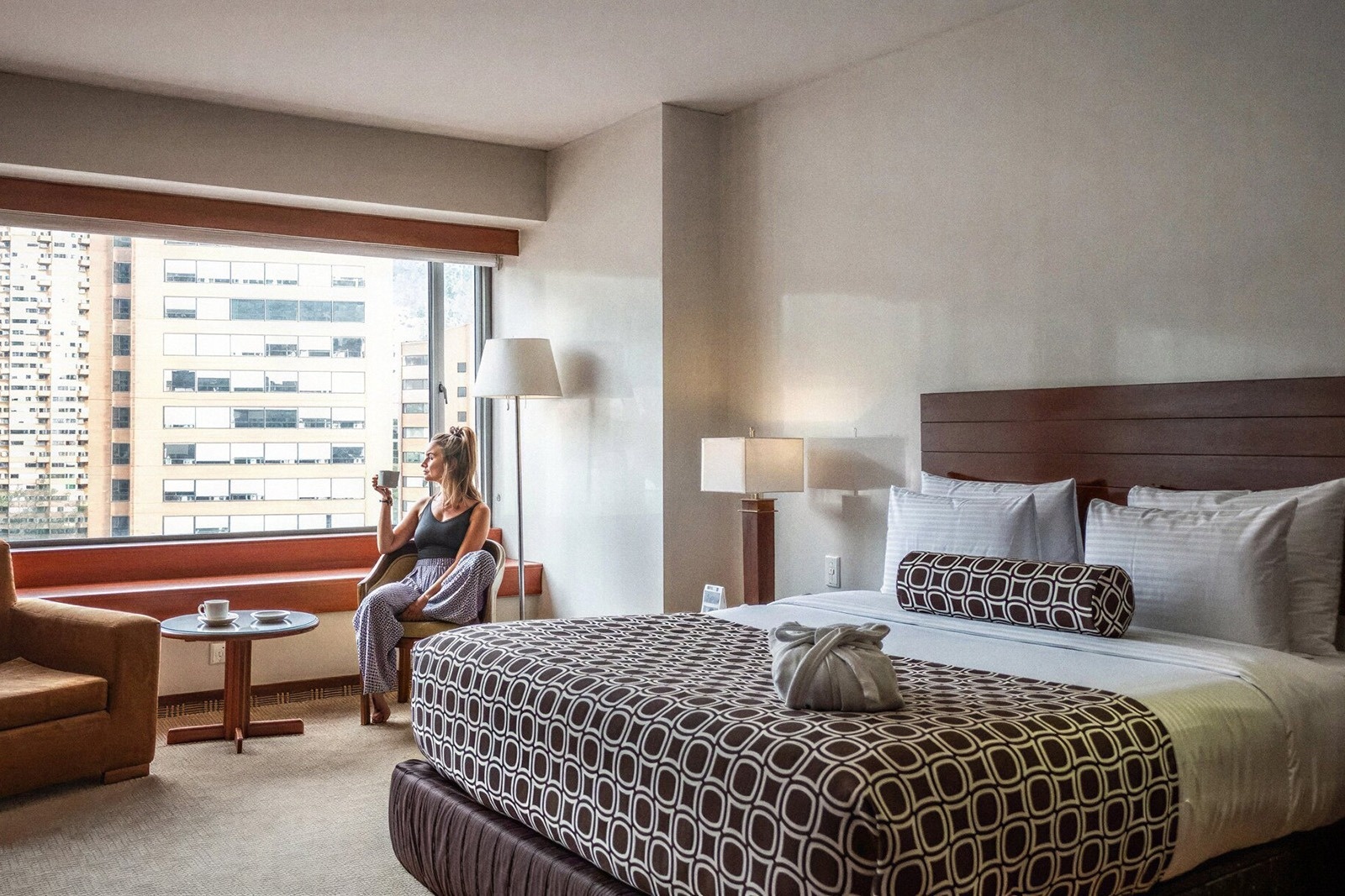 Tequendama Suites Bogotá: Woman with coffee by window in a modern hotel room.