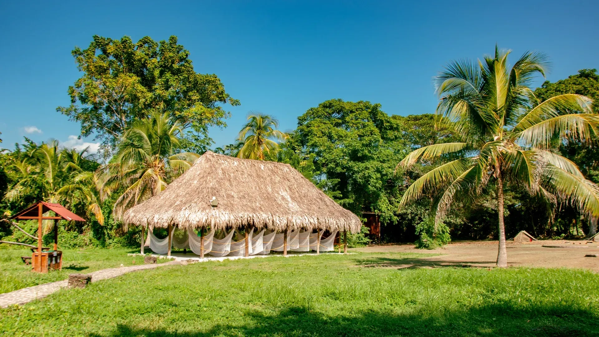 Campings y hamacas en Tequendama, Hotel en Parque Tayrona: cabaña con techo de palma, naturaleza exuberante y cielo azul.