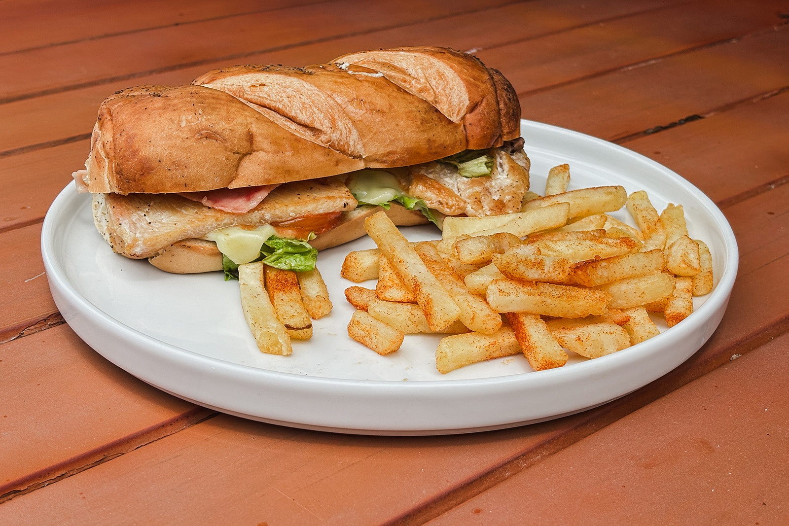 Tecomendama: Corporativa- sándwich de pollo con papas fritas en plato blanco sobre mesa de madera.