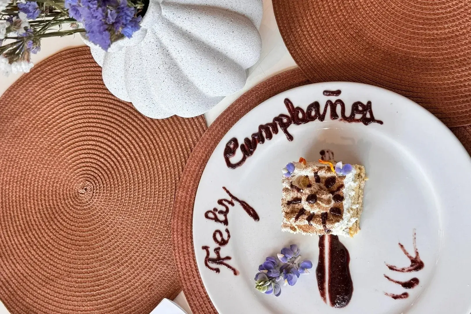 Pastel de cumpleaños en plato blanco con decoraciones de Tequendama: Corporativa y flores.