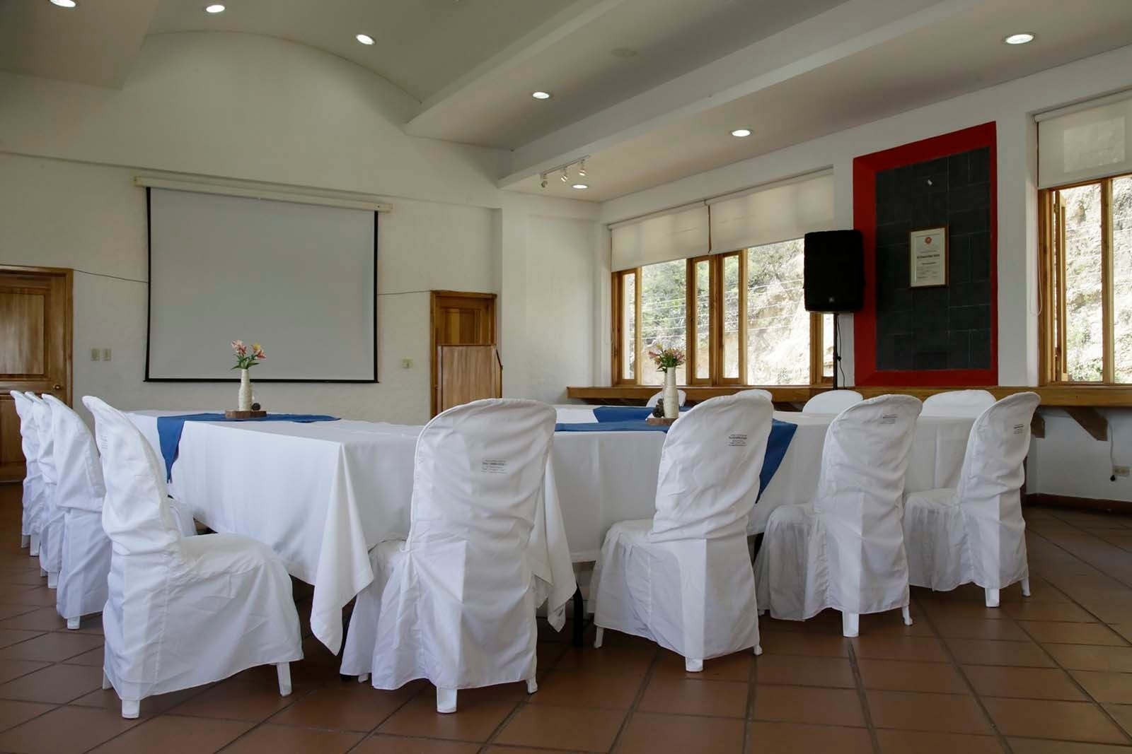 Salón de eventos en Hotel Refugio El Santuario: mesas vestidas y sillas cubiertas, ideal para reuniones.