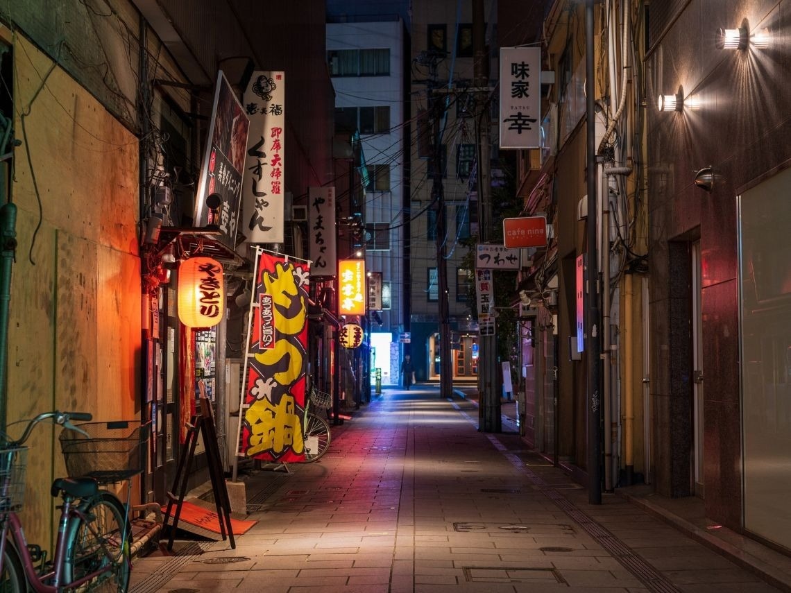 Callejón nocturno japonés con letreros de neón y puestos de comida, ideal para una escapada Tequendama: Corporativa.