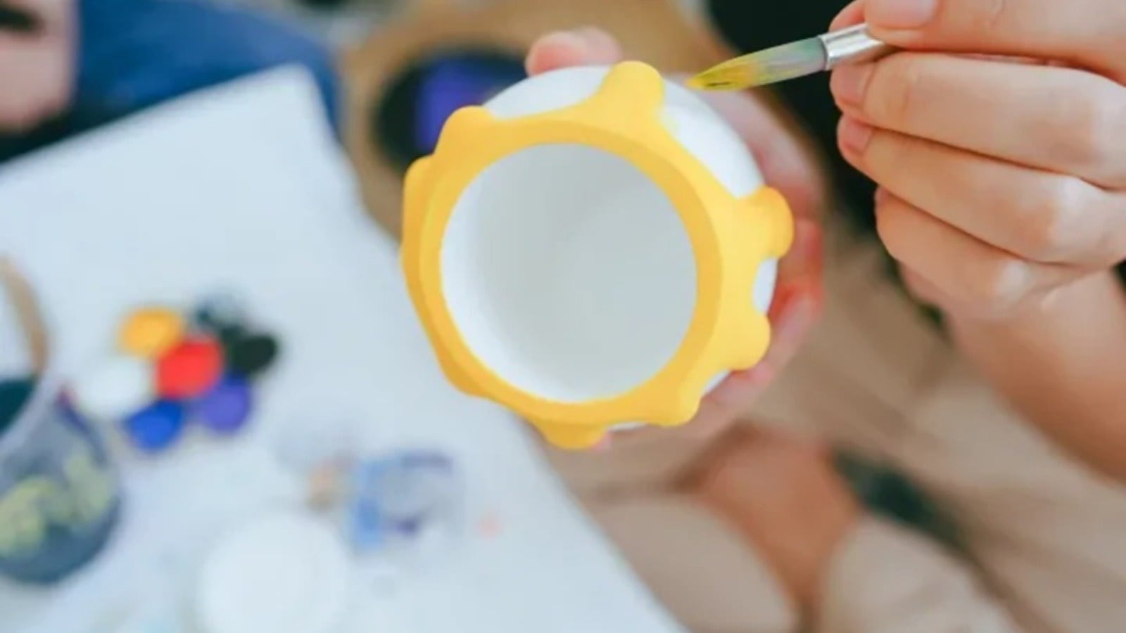 Un primer plano de alguien pintando una bola blanca con adornos amarillos, rodeada de materiales de arte. Hoteles en El Carmen de Viboral.