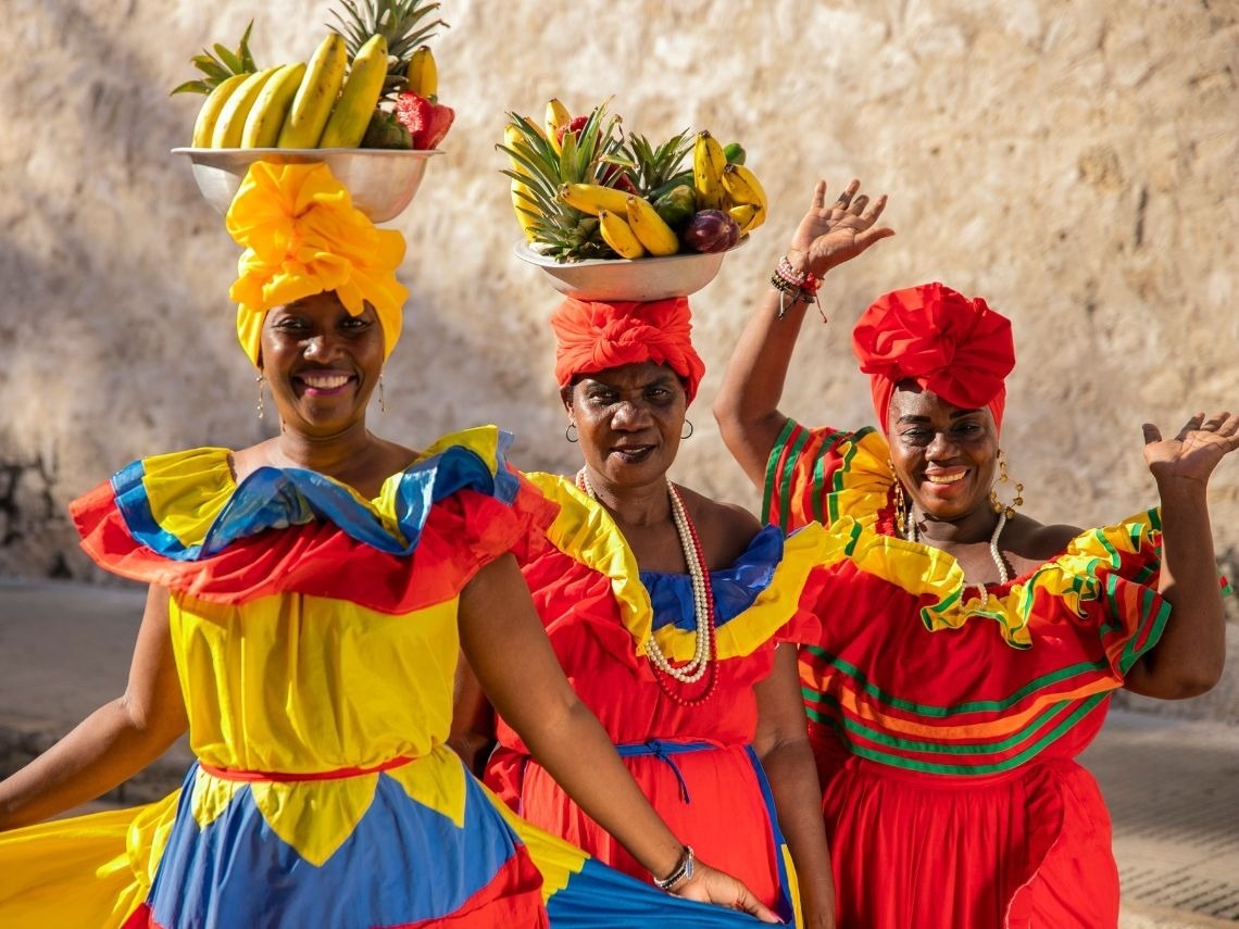 Tres mujeres con vestidos coloridos y turbantes, sonriendo, Tequendama: Corporativa.