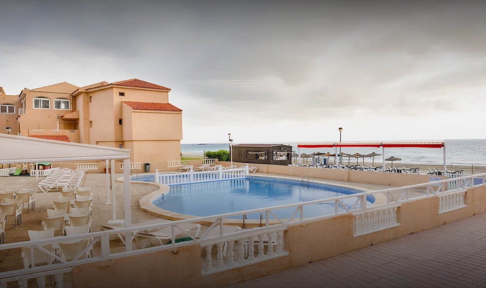 una piscina rodeada de sillas y mesas con vistas al océano