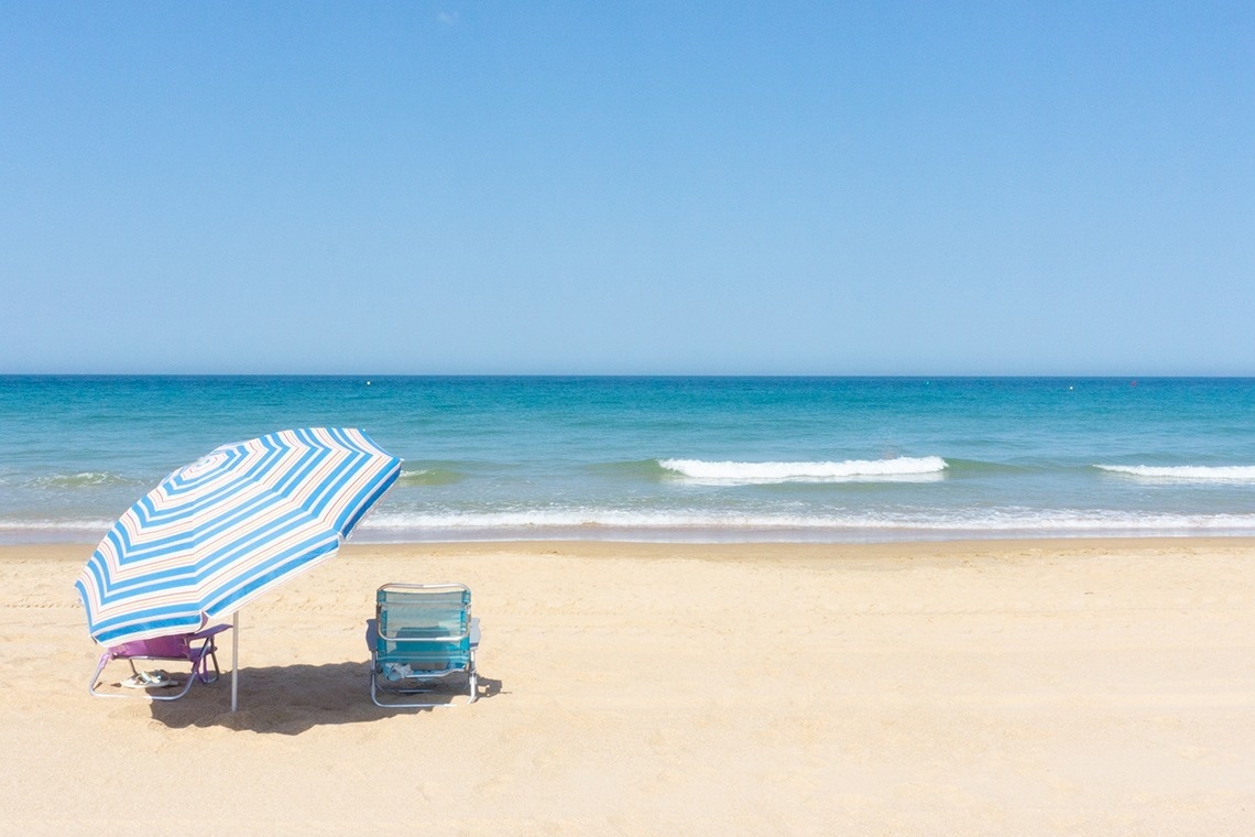 two chairs and an umbrella on a beach with the ocean in the background