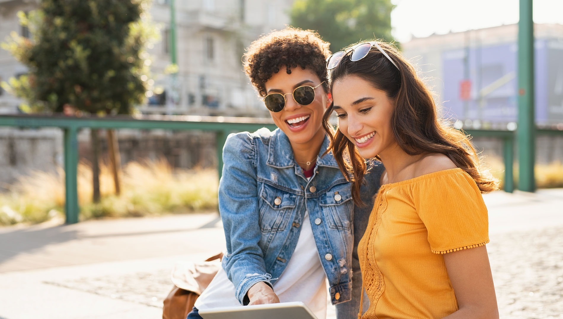 two women are smiling while looking at a tablet