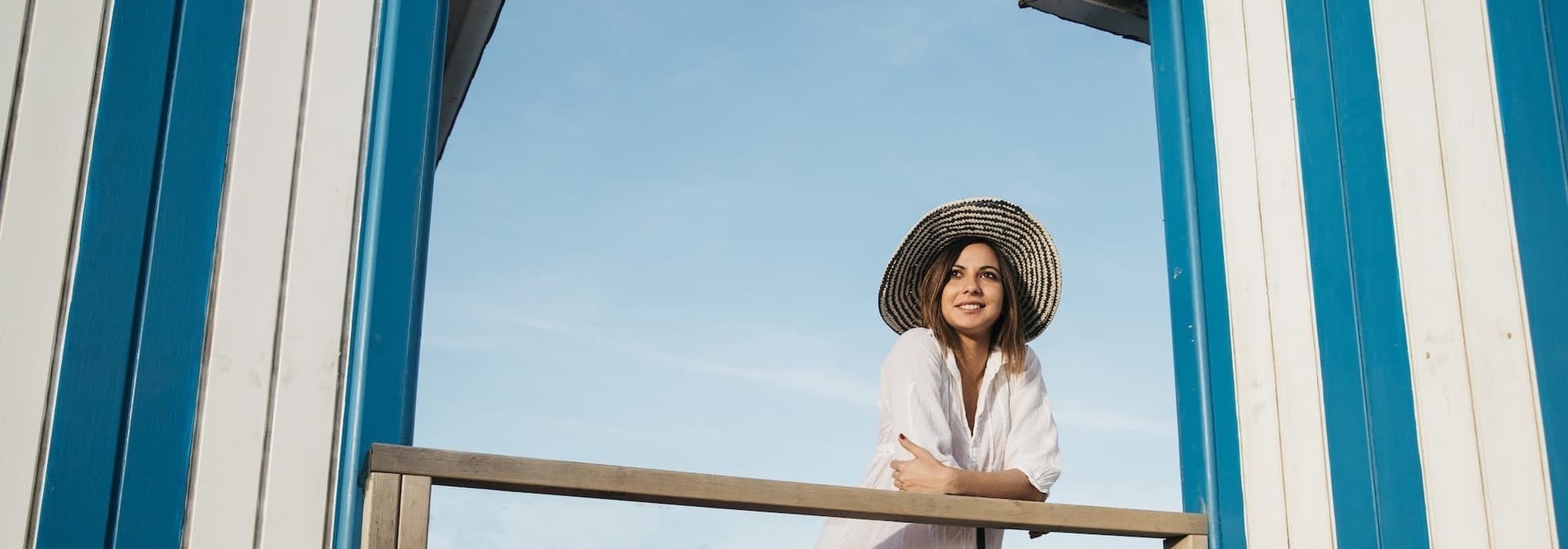 a woman wearing a straw hat stands in front of a blue and white striped building