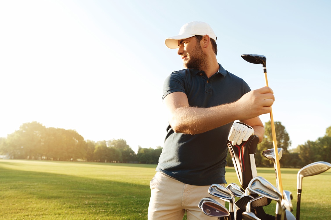 Golfista hombre con bolsa de palos en campo de golf soleado.