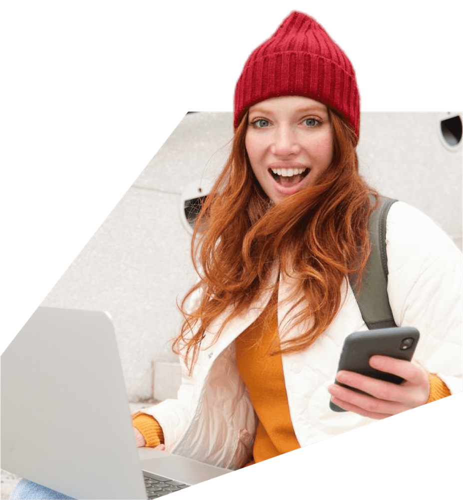 a woman wearing a red beanie is using a laptop and holding a cell phone