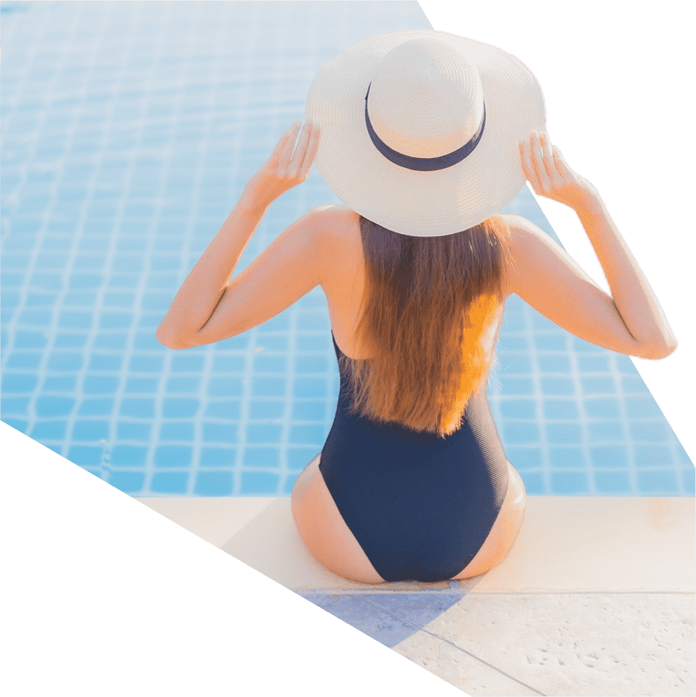 a woman in a swimsuit and hat sits on the edge of a pool