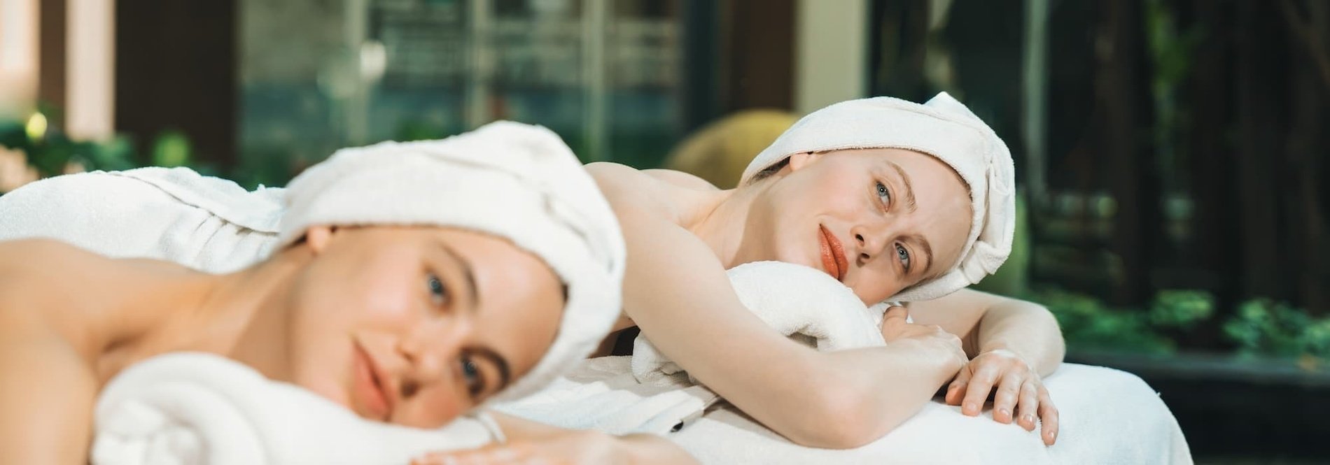 two women wrapped in white towels are laying on a massage table