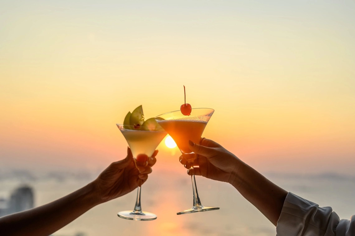 Zwei Cocktails beim Anstoßen bei Sonnenuntergang am Meer