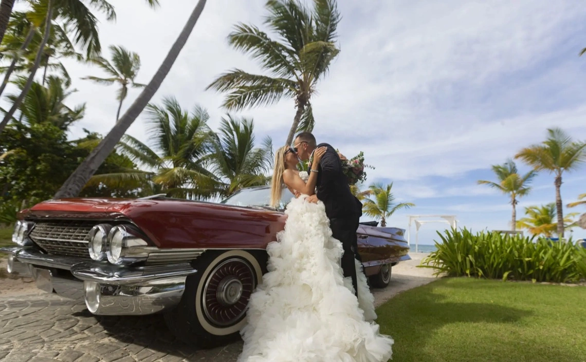 Novios junto a un coche clásico entre palmeras