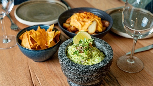 a bowl of guacamole sits next to a bowl of tortilla chips
