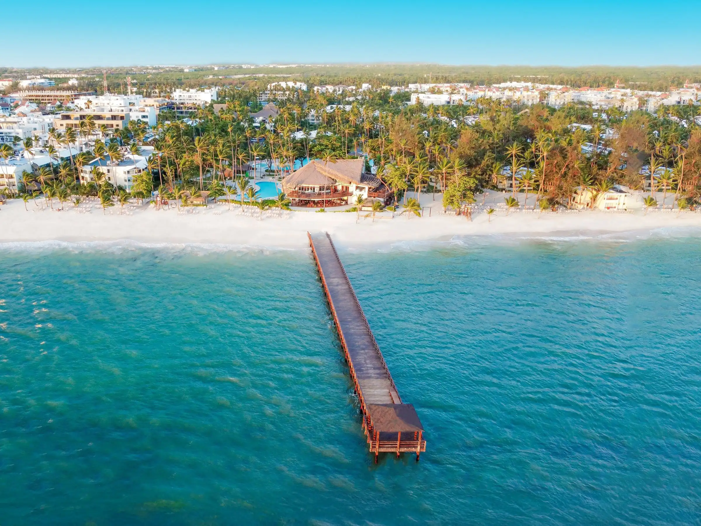 Novios y dama de honor bajo una pérgola en la playa al atardecer