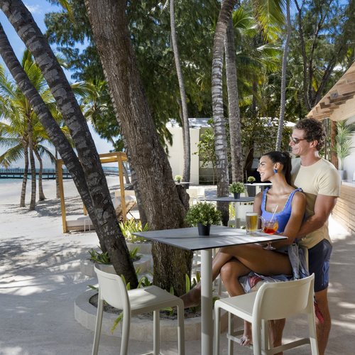 Pareja con cócteles en el beach bar entre palmeras