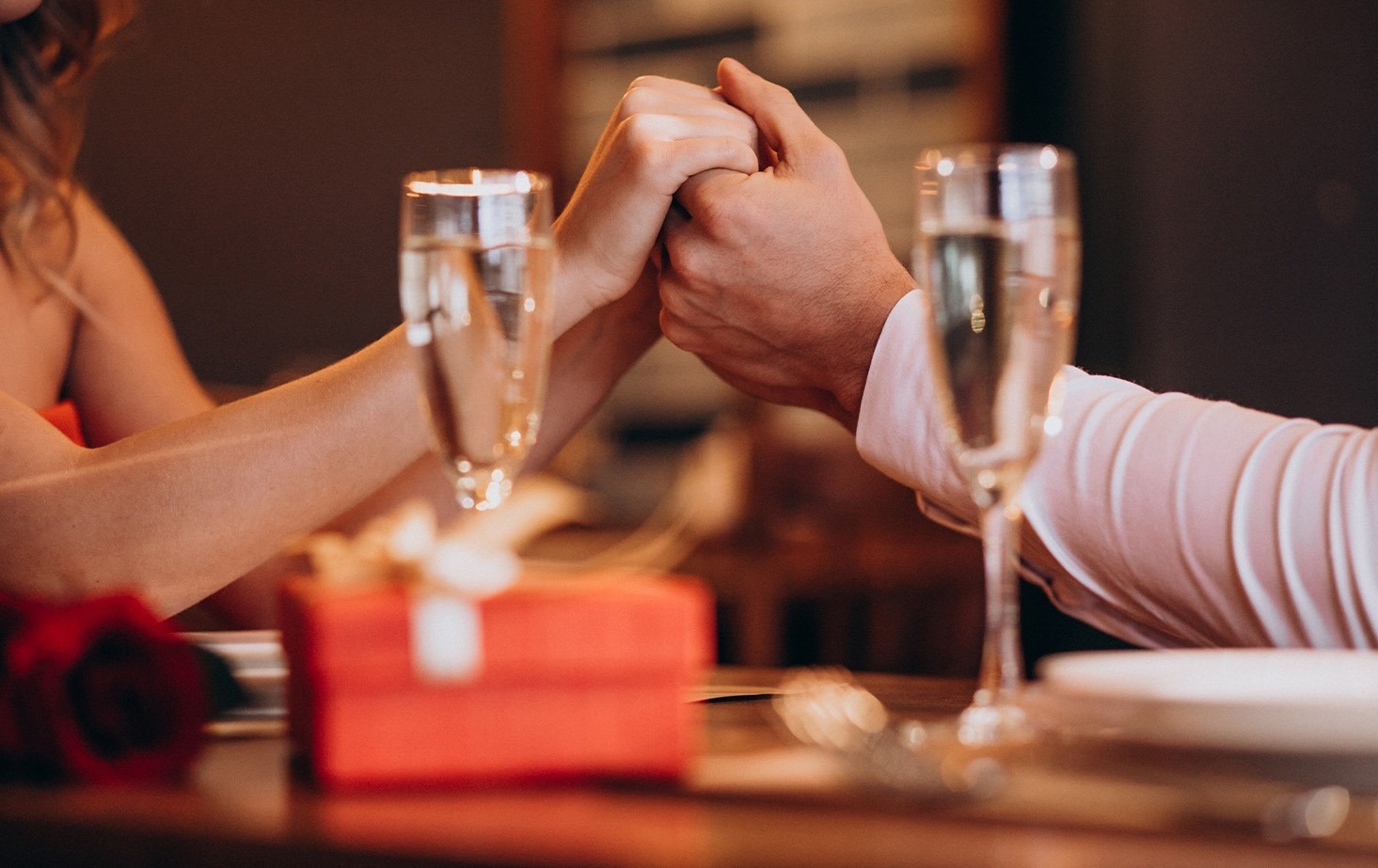 un hombre y una mujer se toman de la mano en una mesa con copas de champán