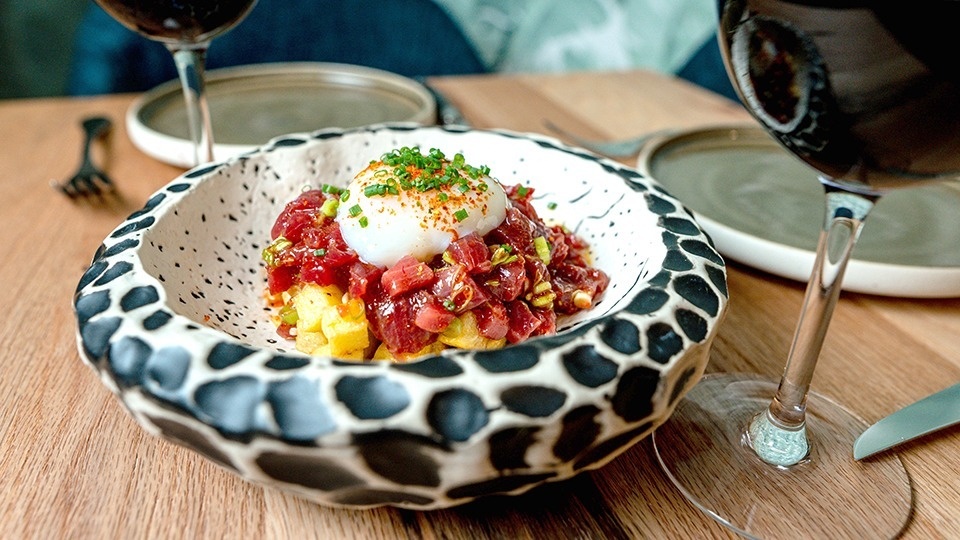 a bowl of food on a table next to a glass of wine