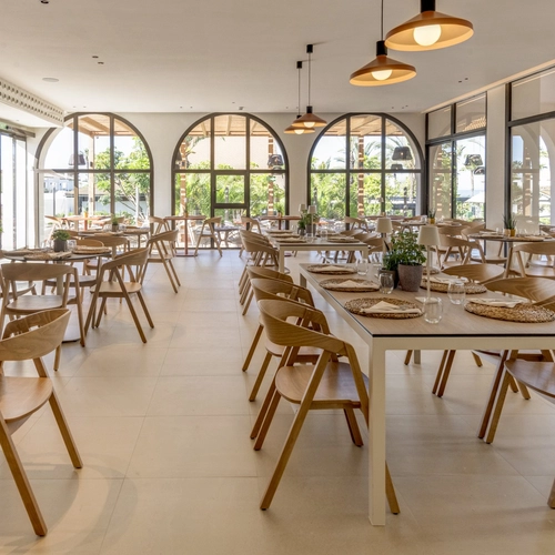 Restaurante con mesas largas de madera y ventanas en arco