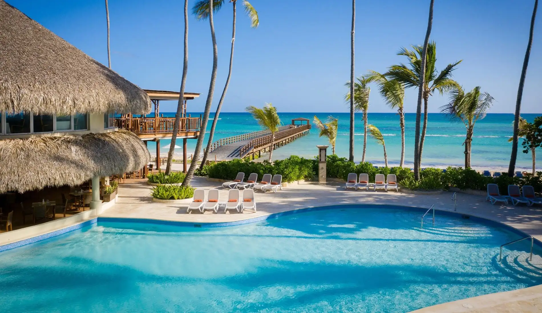 Pool mit Palapa und Palmen vor dem Meer und dem Steg