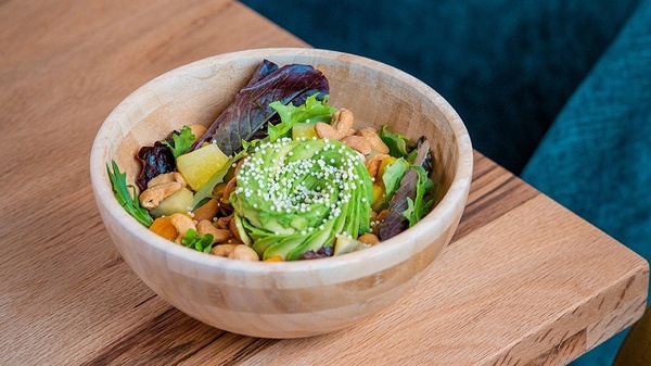 a salad in a wooden bowl with avocado on top