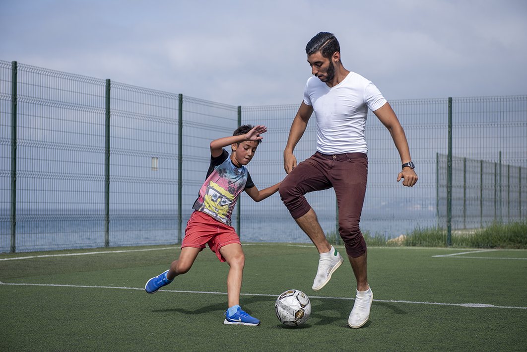 Pai e filho a jogar futebol num campo junto ao mar