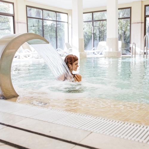 Piscina interior del spa con chorro de agua y tumbonas