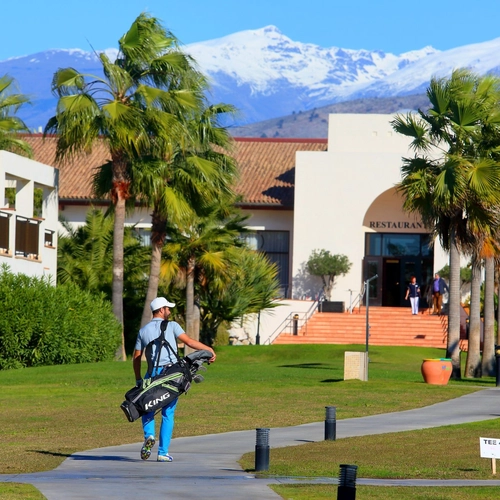 Golfista con su bolsa en los jardines del resort con Sierra Nevada al fondo