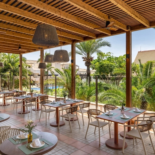 Terraza del restaurante bajo una pérgola de madera con palmeras en Impressive Playa Granada Golf