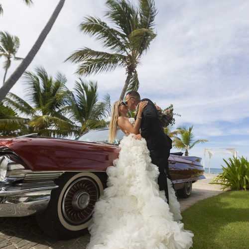 Novios junto a un coche clásico entre palmeras