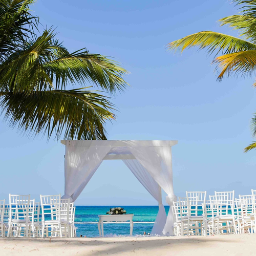 Altar de boda con cortinas blancas y sillas frente al mar entre palmeras