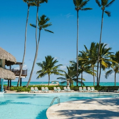 Piscina junto al restaurante con techo de palma y la playa al fondo en Impressive Premium Punta Cana