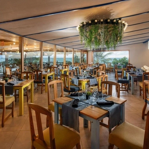 Restaurante de Impressive Punta Cana con mesas de madera y lámpara de plantas