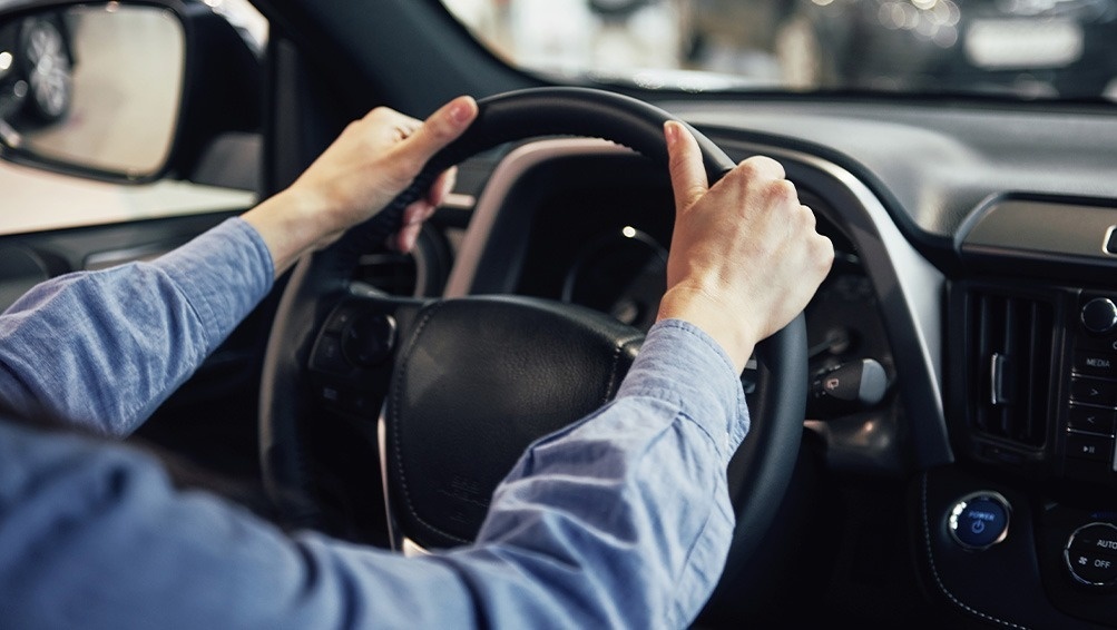 una persona sostiene el volante de un automóvil y el botón de encendido está a la izquierda