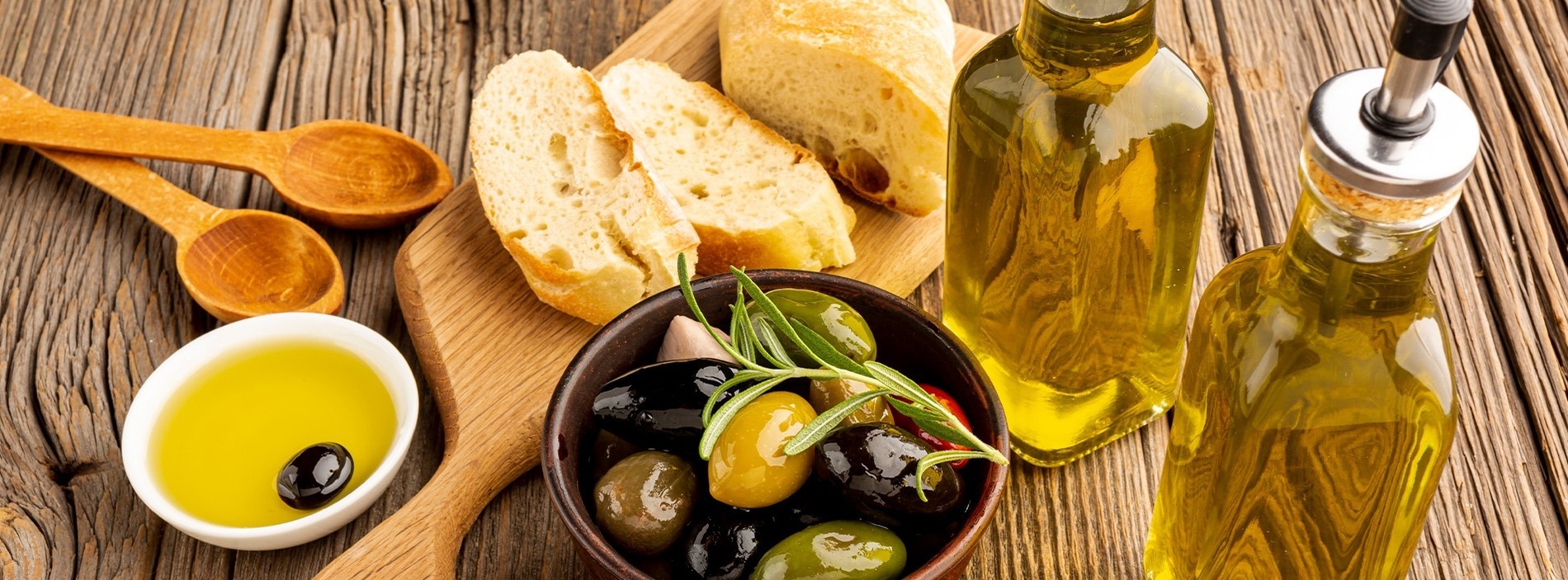 two bottles of olive oil and a bowl of olives on a wooden table