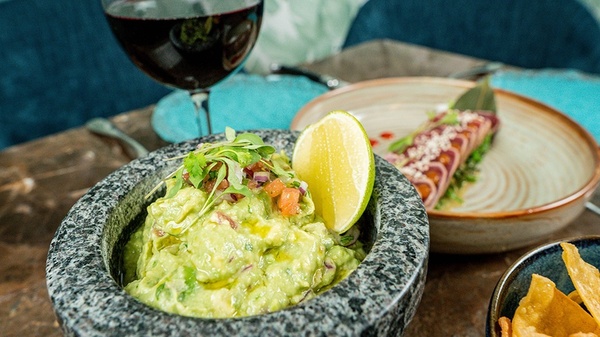 a bowl of guacamole sits on a table next to a glass of wine