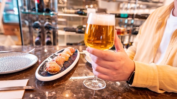 a person holding a glass of beer in front of a plate of food
