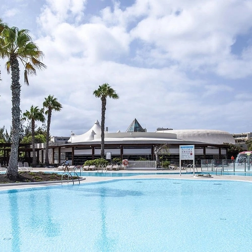 Piscina con palmeras y el edificio de cubiertas blancas de Los Zocos Impressive Lanzarote