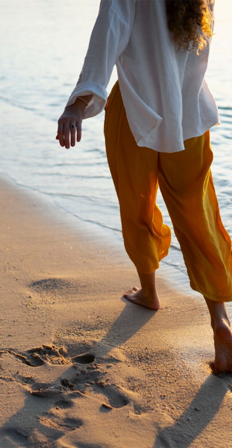 una mujer con pantalones amarillos y una camisa blanca camina por la playa