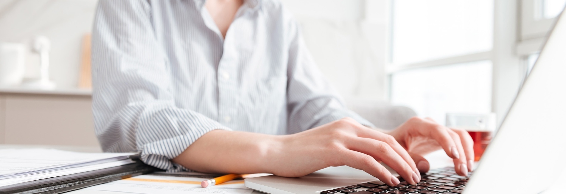 a woman is typing on a laptop with a pencil next to her