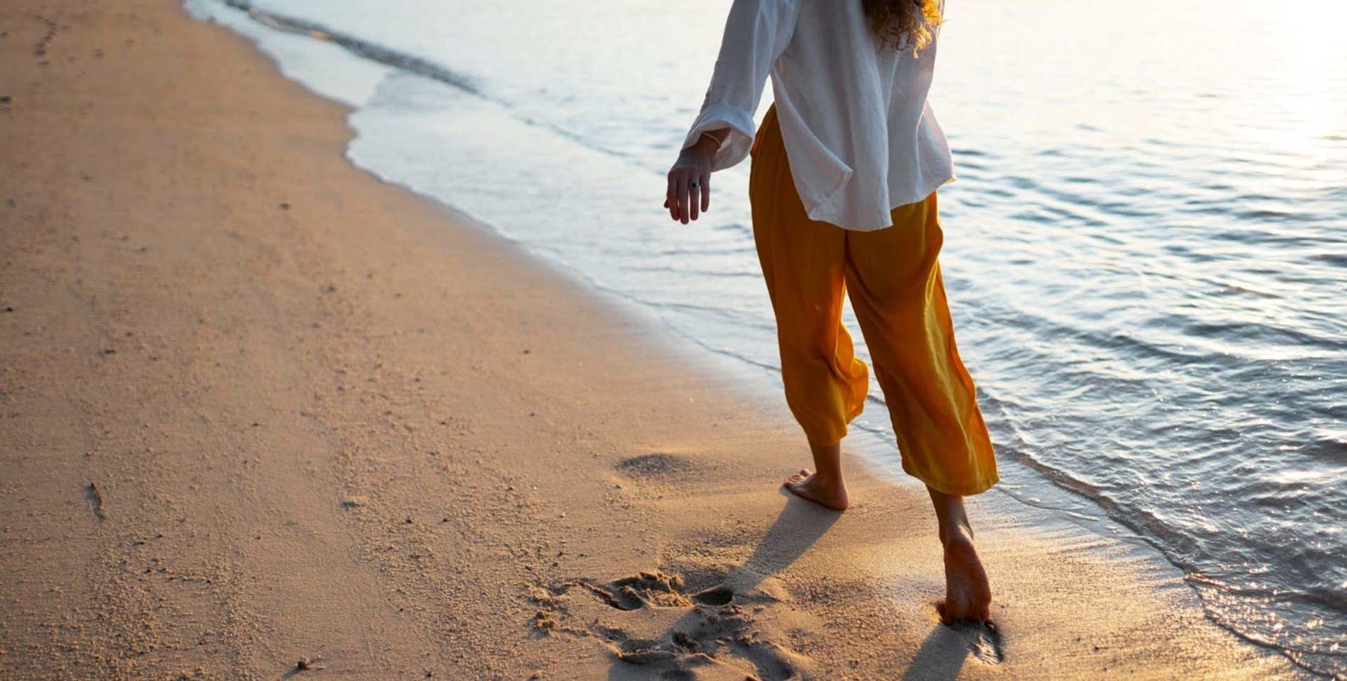 une femme en chemise blanche et pantalon jaune marche sur la plage
